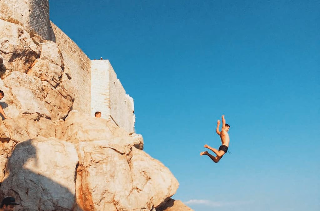 Person cliff jumping into the Adriatic Sea beneath Dubrovnik city walls