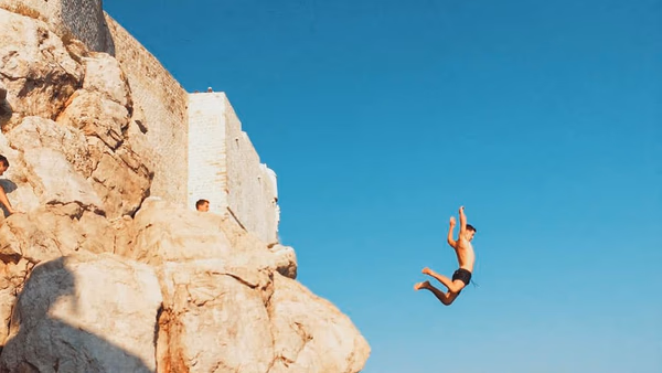 Person cliff jumping into the Adriatic Sea beneath Dubrovnik city walls