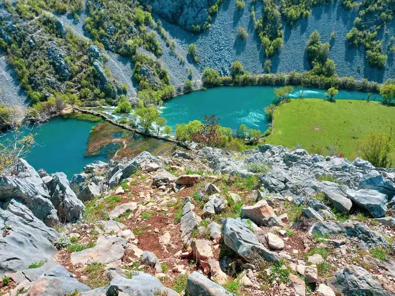 Small travertine waterfalls along the Krupa River with stone footbridges.