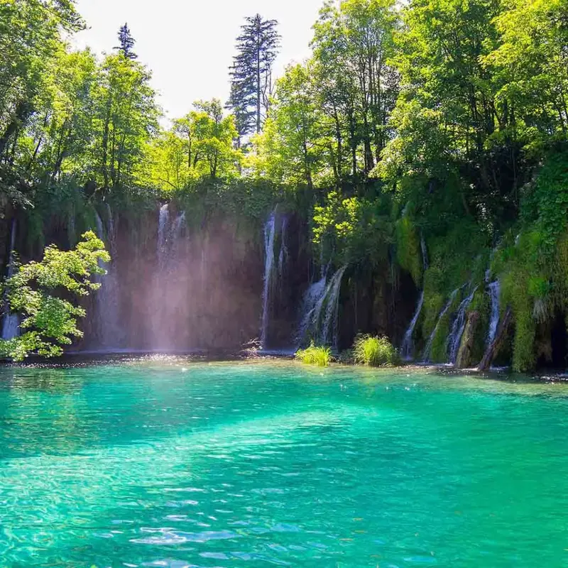 Semi-circular crest waterfall dropping into a clear Plitvice pool.