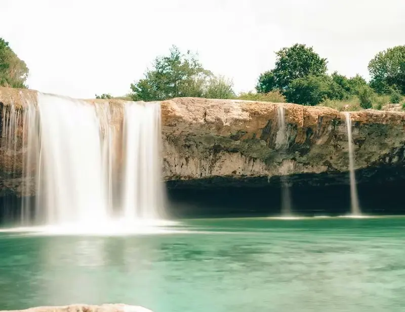 Waterfall plunging from a rocky overhang (cave roof) into a deep pool.