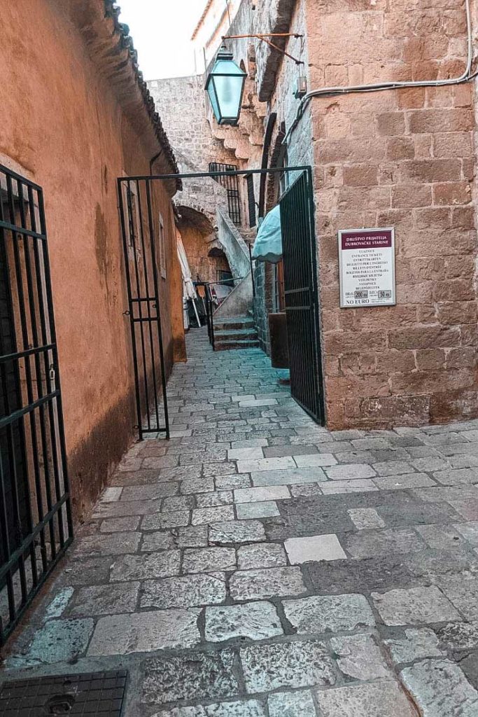 Narrow cobbled passage with gates and sign at the Ploče Gate City Walls entrance.